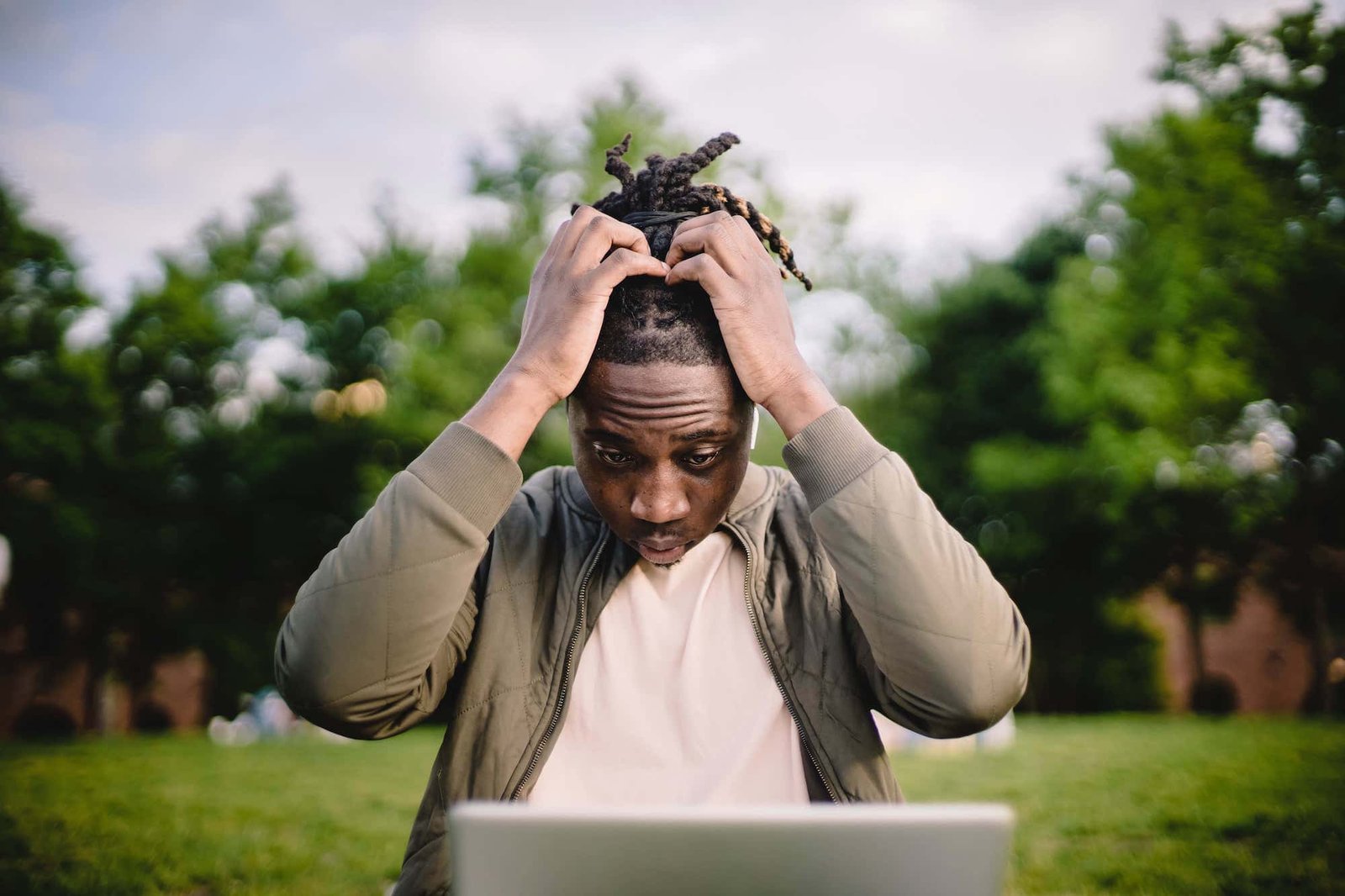 A person sitting outside, looking at a laptop with a concerned expression, holding their head with both hands—perhaps frustrated by common web design mistakes. Trees and grass are visible in the background.