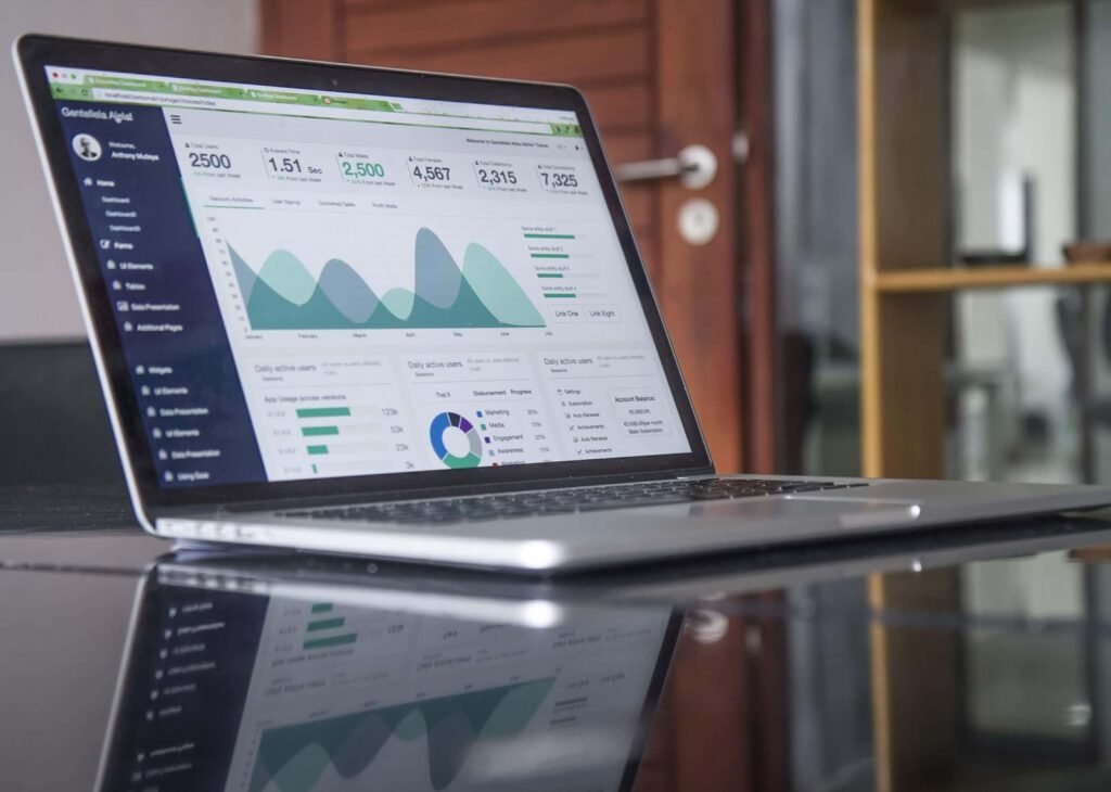 A laptop on a glass table displays a business analytics dashboard with graphs, charts, performance metrics, and seo insights.