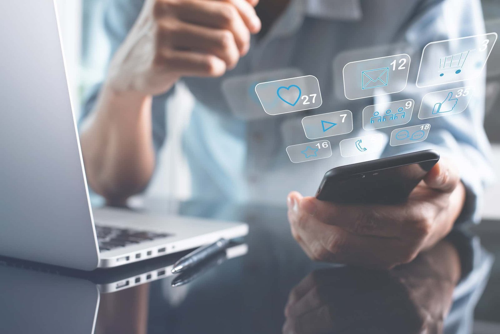 A person holds a smartphone near a laptop, with digital icons for social media notifications, messages, and shopping overlayed above the phone, highlighting the importance of SEO in today’s connected digital landscape.