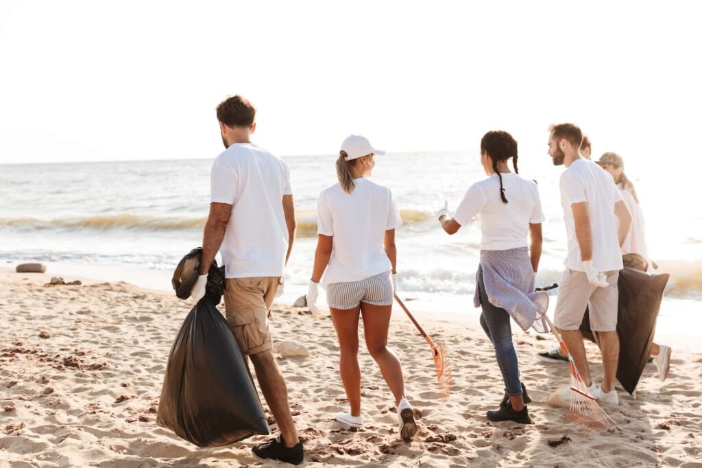 Empower Your Nonprofit with Outstanding Web Design and Targeted SEO Strategies A group of people from a nonprofit, wearing white shirts, pick up trash and rake debris on a sandy beach near the ocean.
