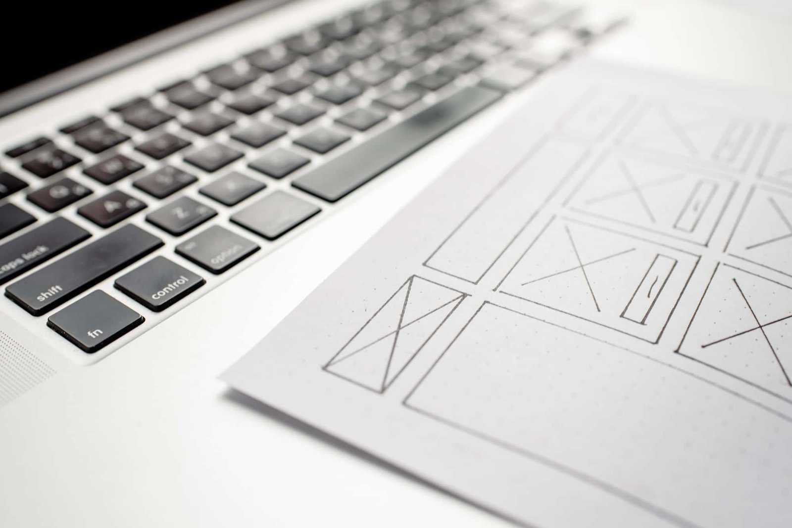A sheet of website wireframe sketches rests on a laptop keyboard, illustrating layout plans for a digital Health and Wellness interface.
