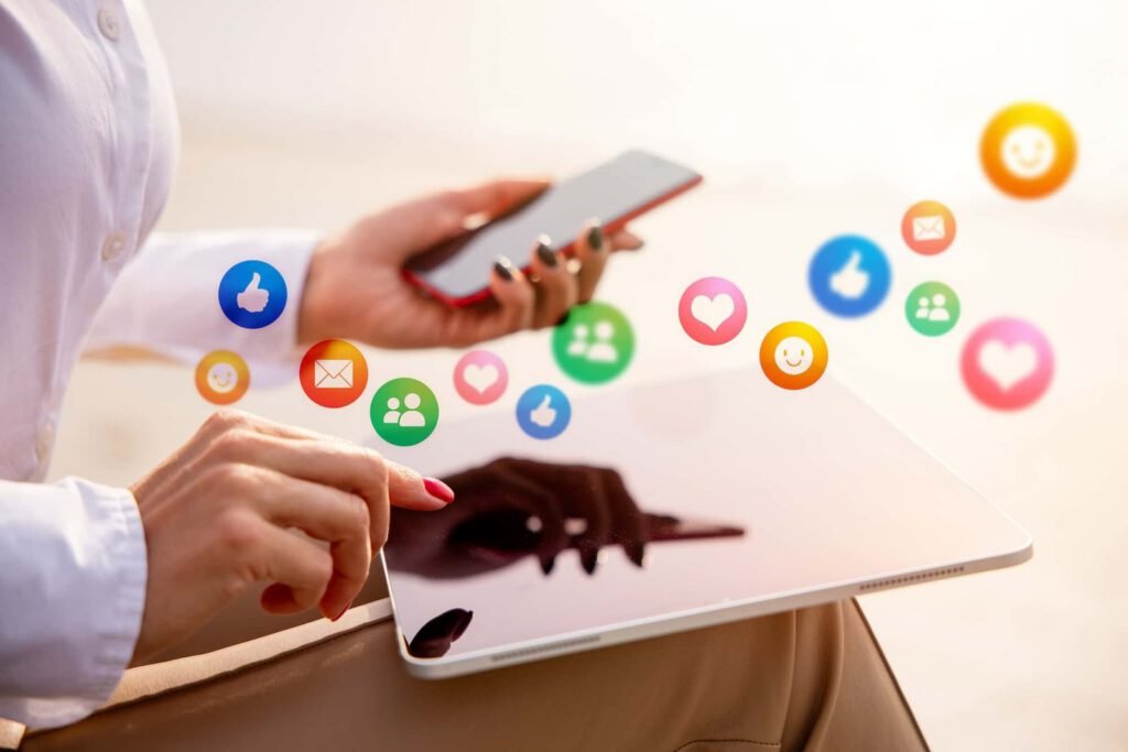 A person uses a tablet and holds a smartphone, with colorful social media icons appearing above the devices.
