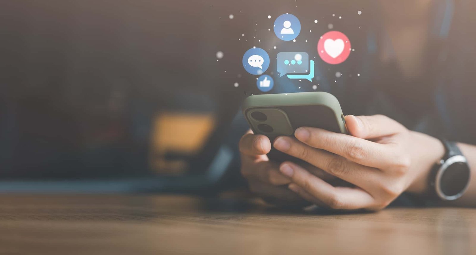 Hands holding a smartphone with floating social media icons, including like, comment, chat, and heart symbols, above the device.