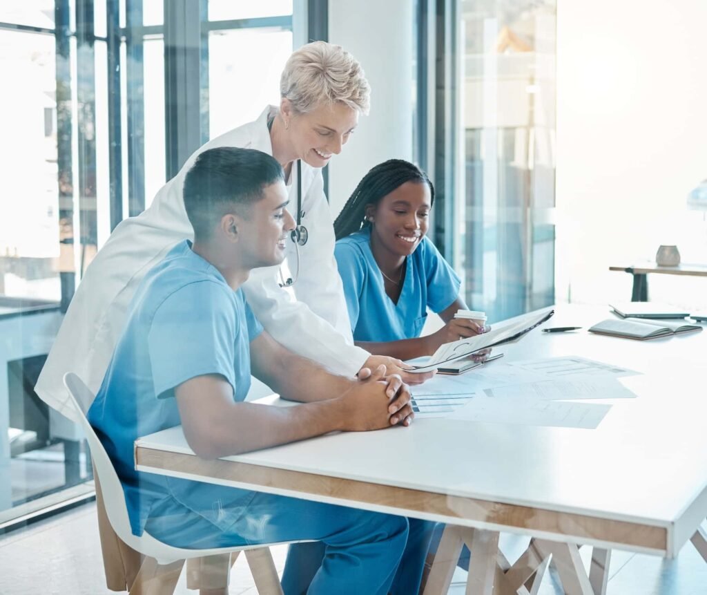 Web Design for Healthcare: 10 Essential Features You Can't Ignore Three medical professionals, two seated and one standing, review documents and take notes at a table in a bright, modern office—collaborating on best practices like those found in "Web Design for Healthcare: 10 Essential Features You Can't Ignore.