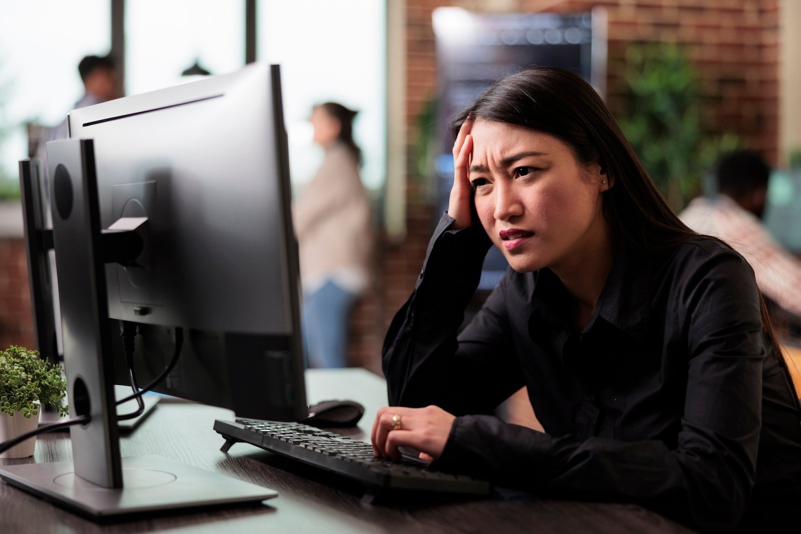 A woman sits at a desk, looking frustrated while staring at a computer monitor, concerned about low conversions, with her hand on her forehead.