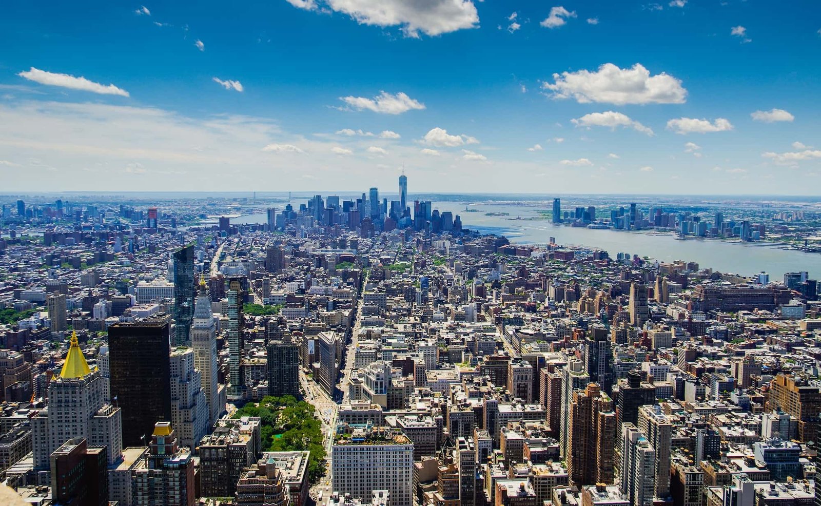 Aerial view of Manhattan, NYC, showing skyscrapers, dense buildings, and rivers on a clear, sunny day.