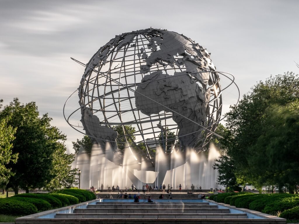 A large metal globe sculpture with rings stands surrounded by water fountains and trees in an outdoor park setting, offering inspiration much like the creative spark behind top web design tips for Queens entrepreneurs.