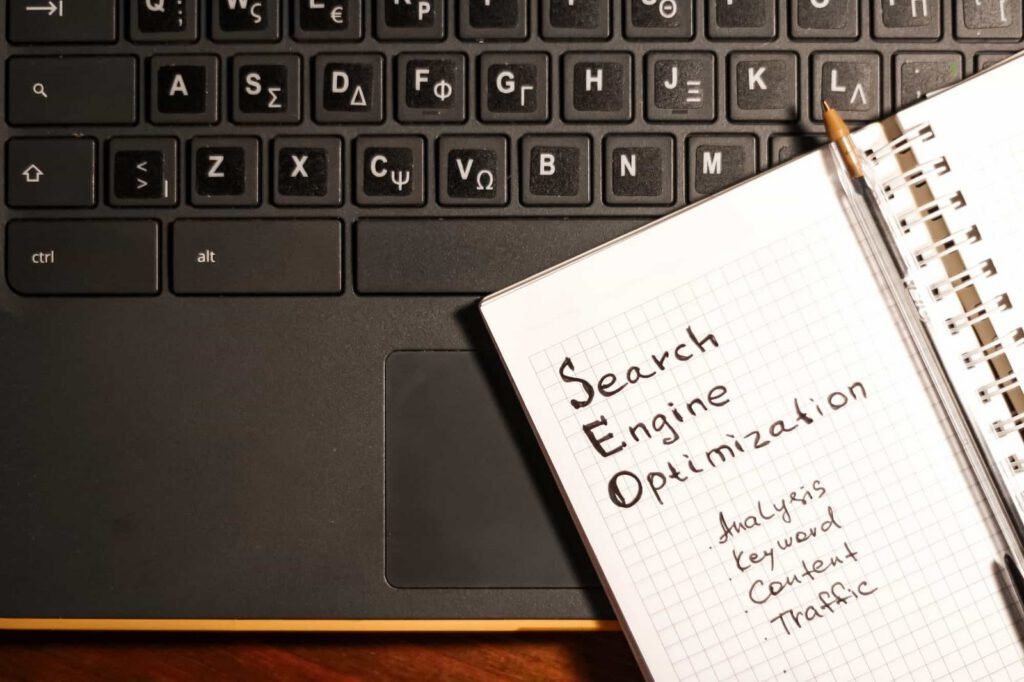 A notebook labeled "SEO Search Engine Optimization" with related keywords rests on a laptop keyboard with both English and Greek letters. 10 Essential Tips for Building a WordPress Site with SEO in Mind