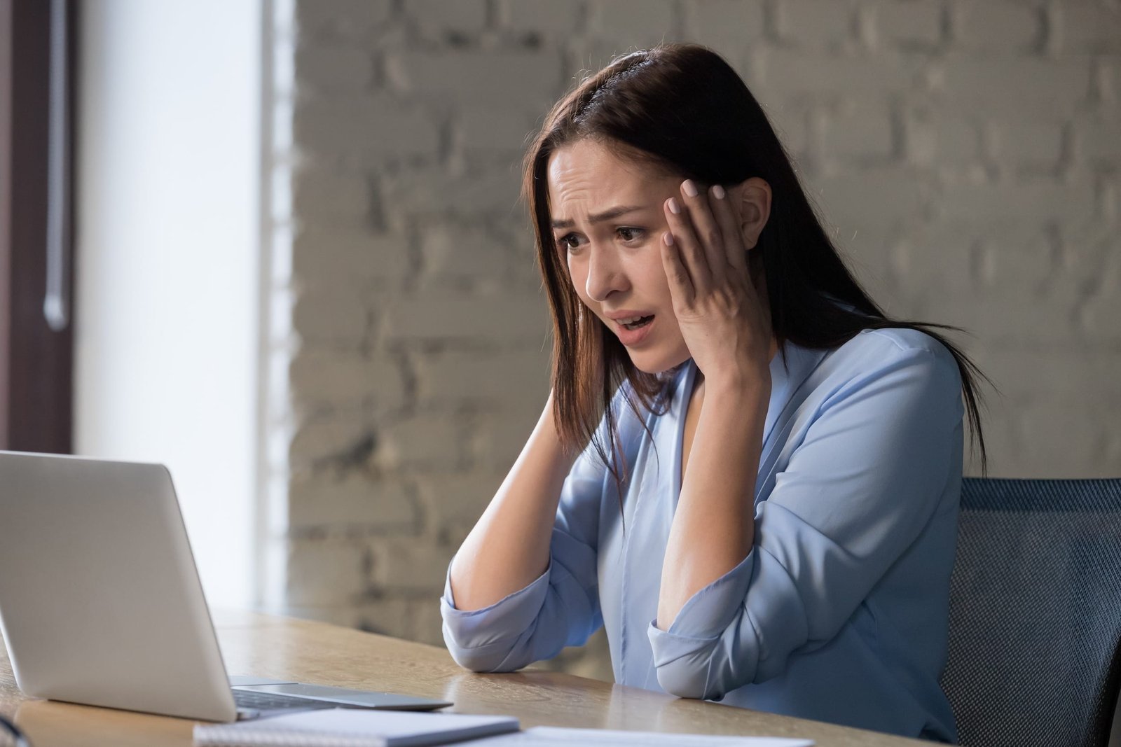 A woman sits at a desk looking at a laptop with a worried expression, holding her head with both hands. The Hidden Costs of Using Wix and Squarespace for Your Business
