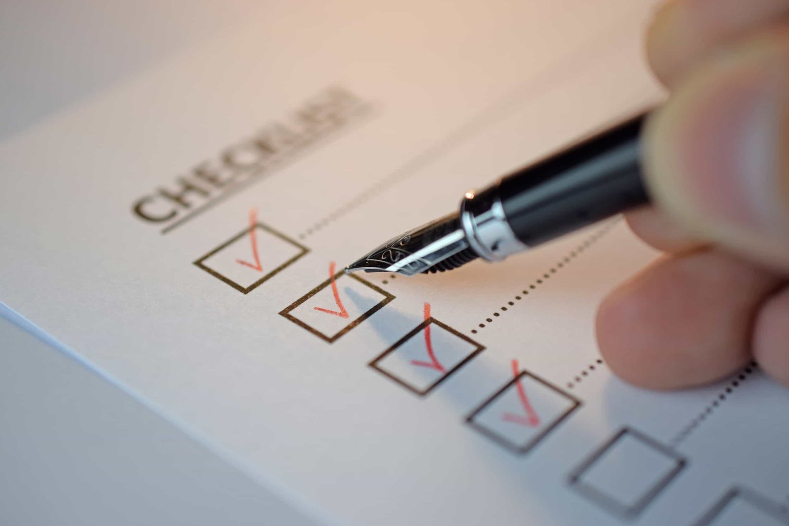 A hand holding a pen checks off boxes on a paper checklist, with several boxes already marked with red checkmarks. The Simple SEO Checklist for Small Business Websites