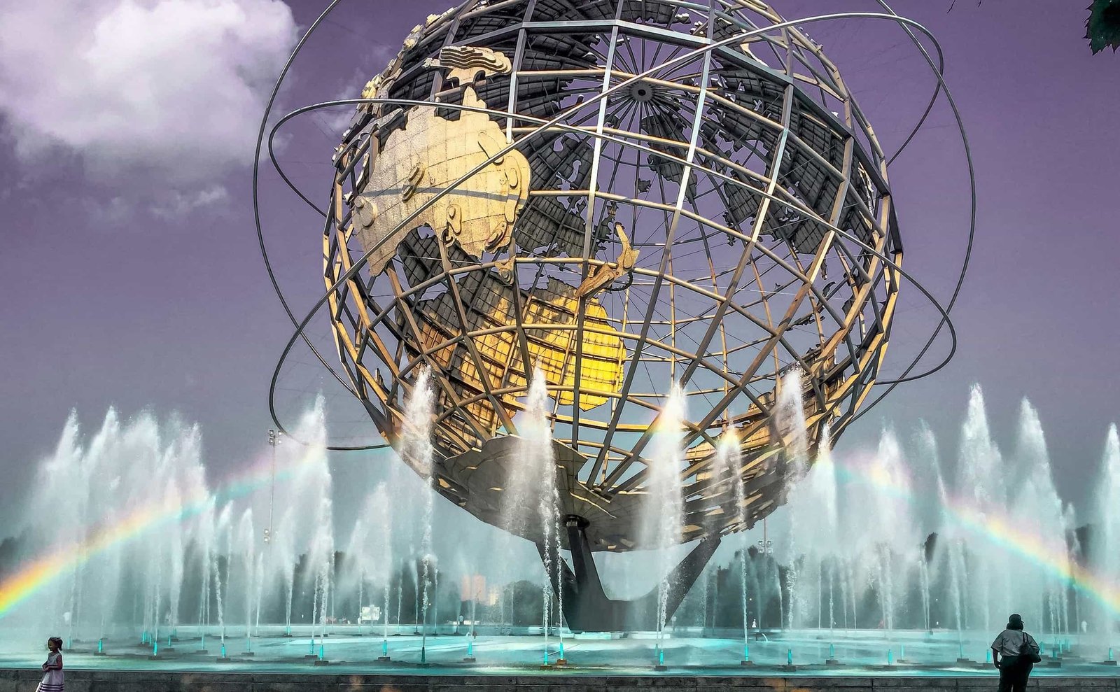 Large metal globe sculpture surrounded by fountains, with a faint rainbow and people walking nearby under a purple sky—a scene as vibrant as the Web Design and SEO in Queens community.