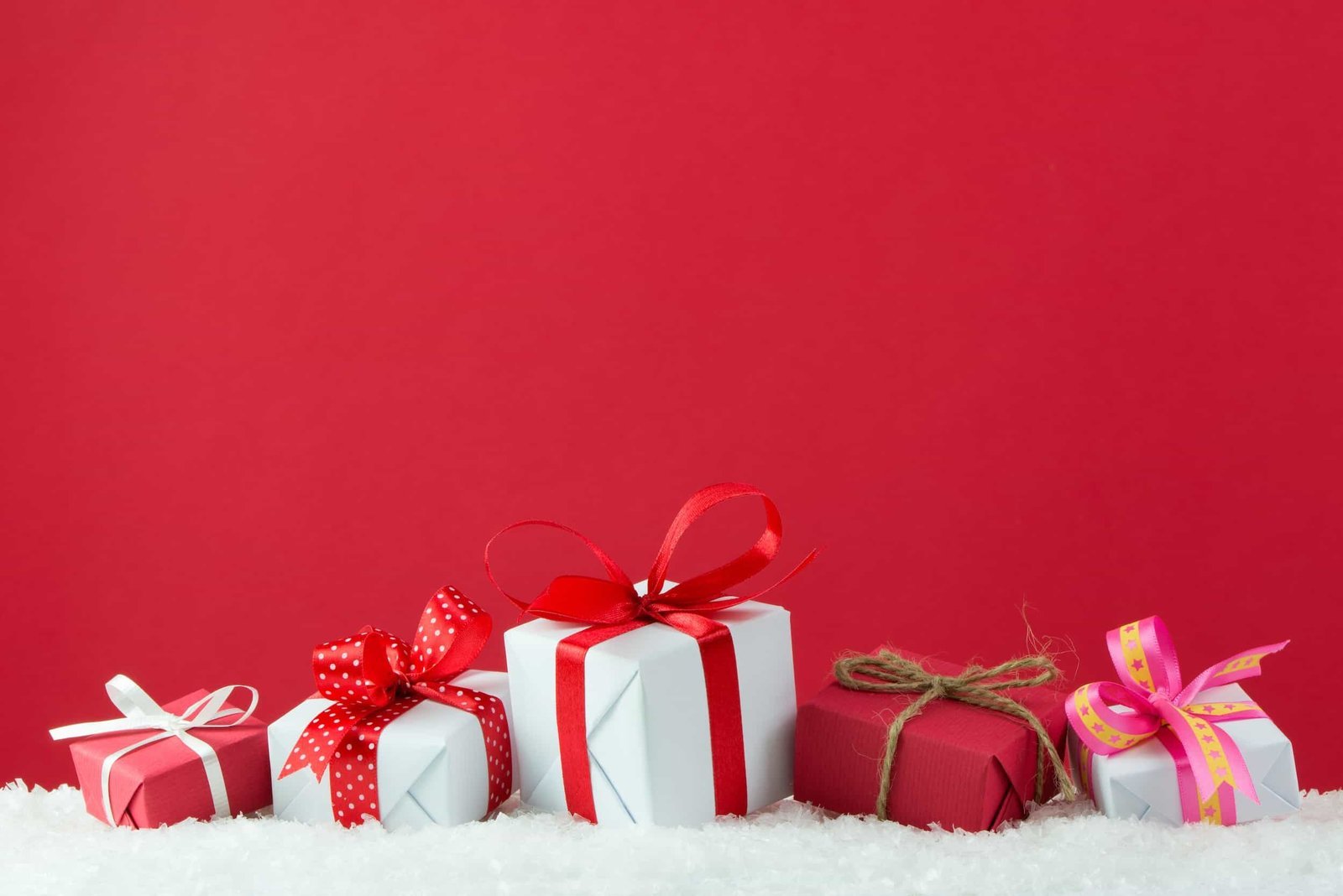 Five wrapped gift boxes with red and white ribbons and bows are arranged on a layer of artificial snow against a plain red background. Discover essential tips to optimize your WordPress site for Black Friday 2025. Boost traffic and sales with our comprehensive guide.
