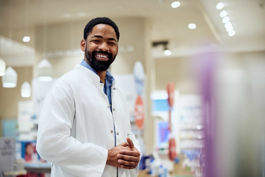 How to Get Leads for Pharmaceuticals: Top Marketing Strategies A man wearing a white lab coat stands smiling in a brightly lit pharmacy or medical store. Pharmaceutical