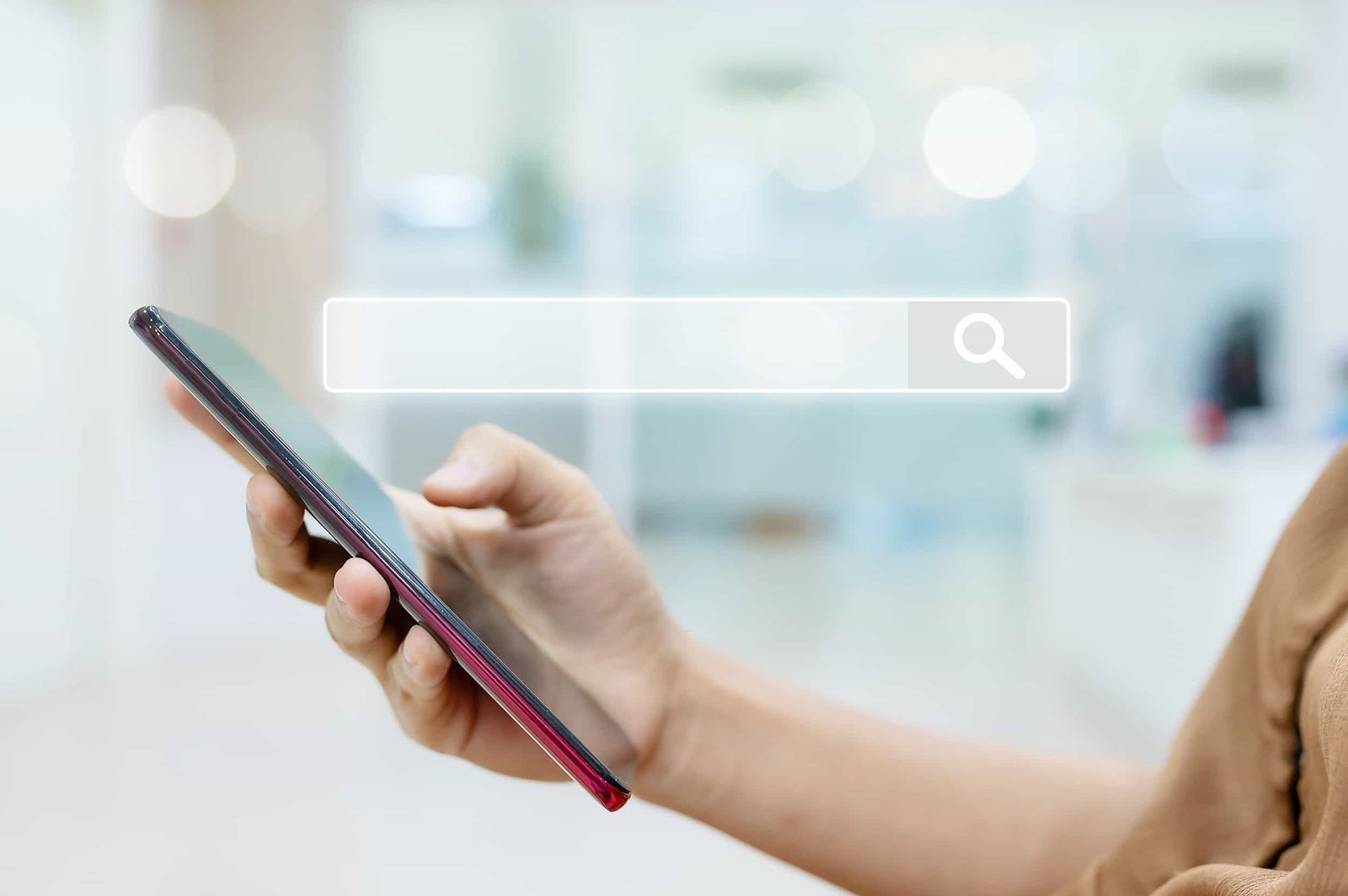 A person holds a smartphone with their thumb on the screen. A graphics of a search bar with a magnifying glass icon is superimposed above the phone. SEO in 2026