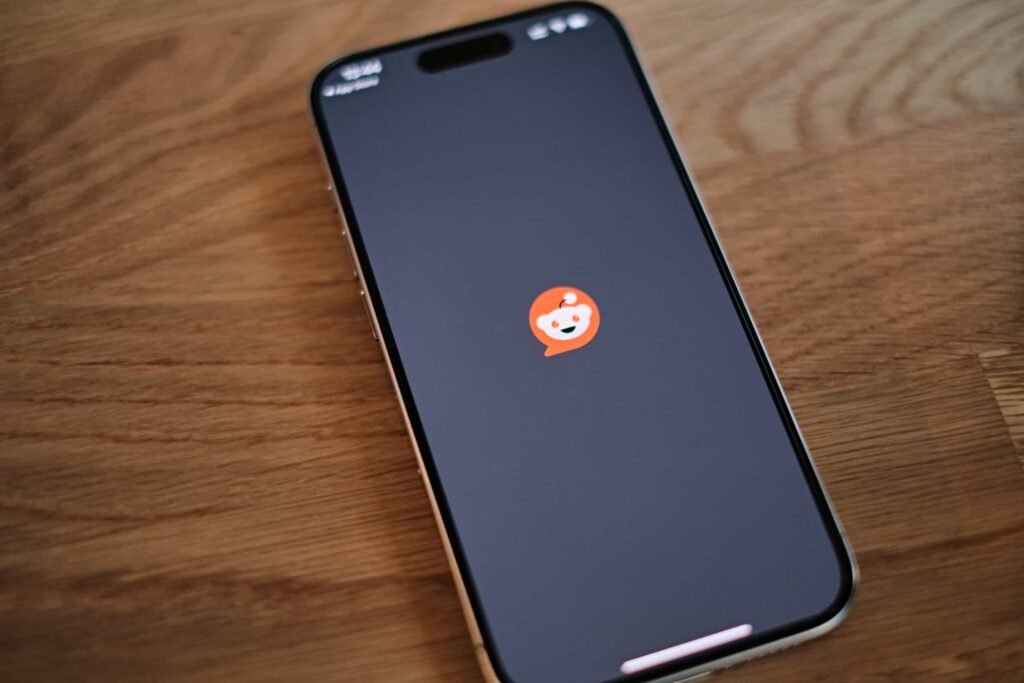 A smartphone with the Reddit app loading screen displayed, placed on a wooden surface. Why Google Ranks Reddit Threads Above Your Website.