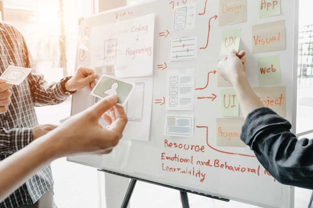 Three people collaborate by placing cards and sticky notes on a whiteboard covered with diagrams and project planning notes related to UX, web, and app design. Why Most SEO Strategies Fail Before They Start
