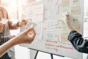 Three people collaborate by placing cards and sticky notes on a whiteboard covered with diagrams and project planning notes related to UX, web, and app design. Why Most SEO Strategies Fail Before They Start