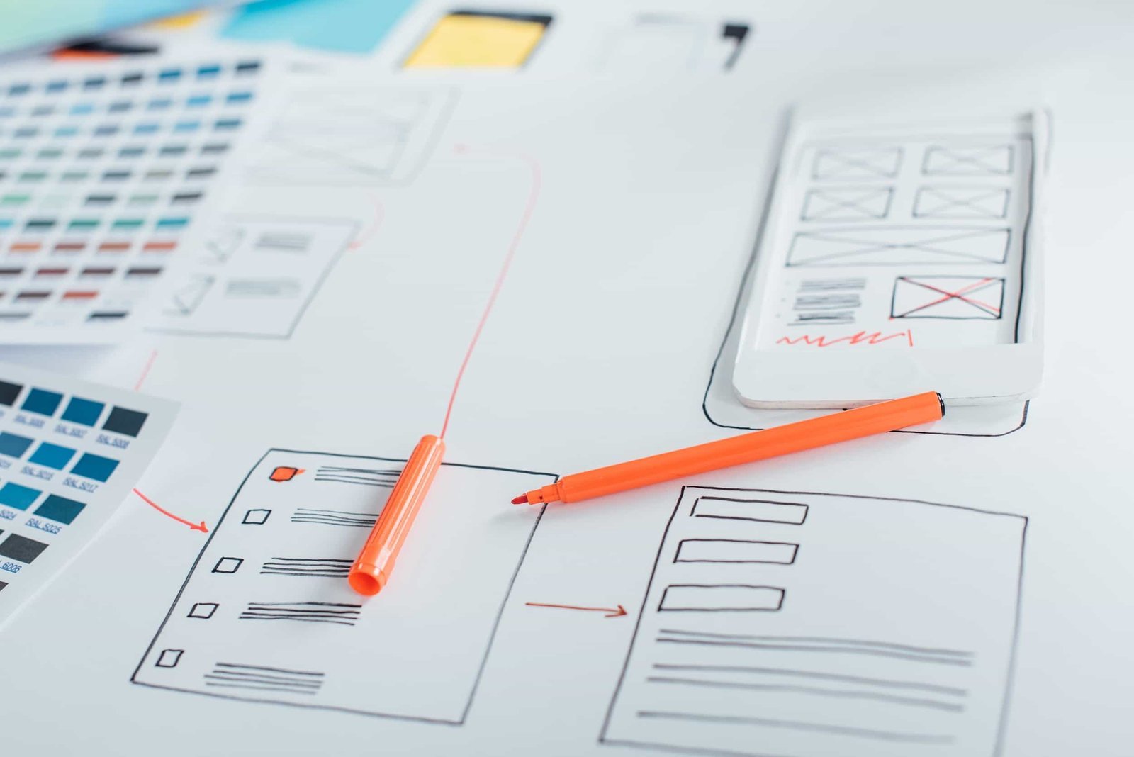 A table with website wireframe sketches, an orange pen, and a smartphone mockup next to printed color swatches. Why Professional Web Design Beats DIY Every Time.
