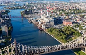 Aerial view of a power plant with tall smokestacks beside a river, surrounded by urban buildings and bridges in a city landscape—perfect for showcasing local SEO efforts within industrial city environments.