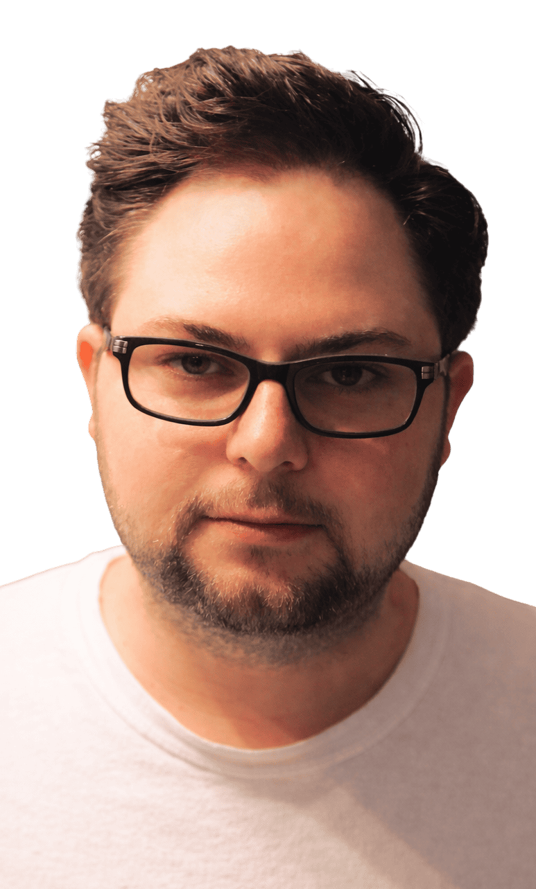 A man with short brown hair, glasses, and a trimmed beard is wearing a light-colored shirt and facing the camera against a plain background.