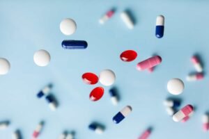 Various pills and capsules in different shapes and colors are suspended against a light blue background. pharmaceutical nyc