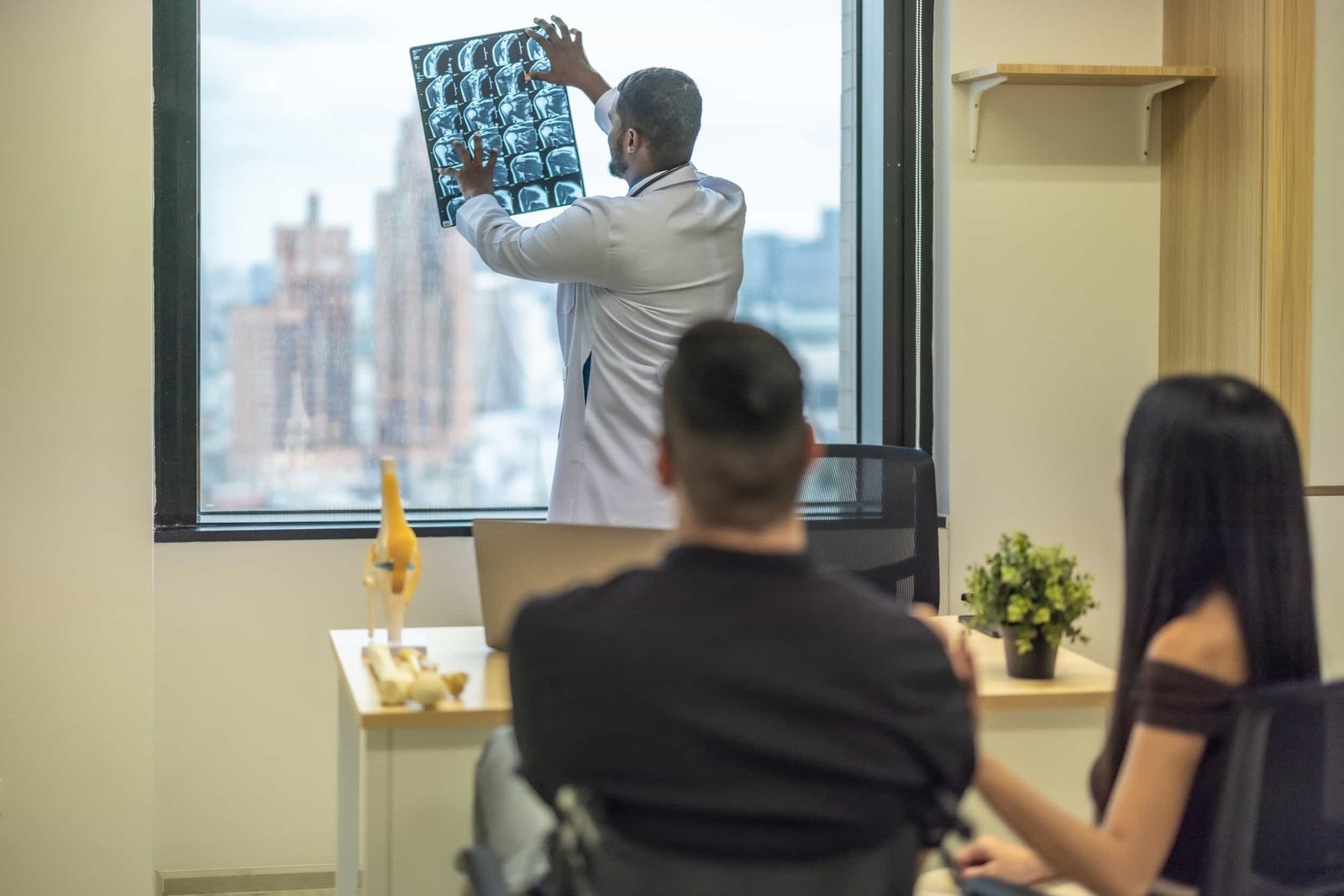 A doctor examines X-ray images by a window, while two patients sit across from him in a medical office that can easily be found on Google Maps.