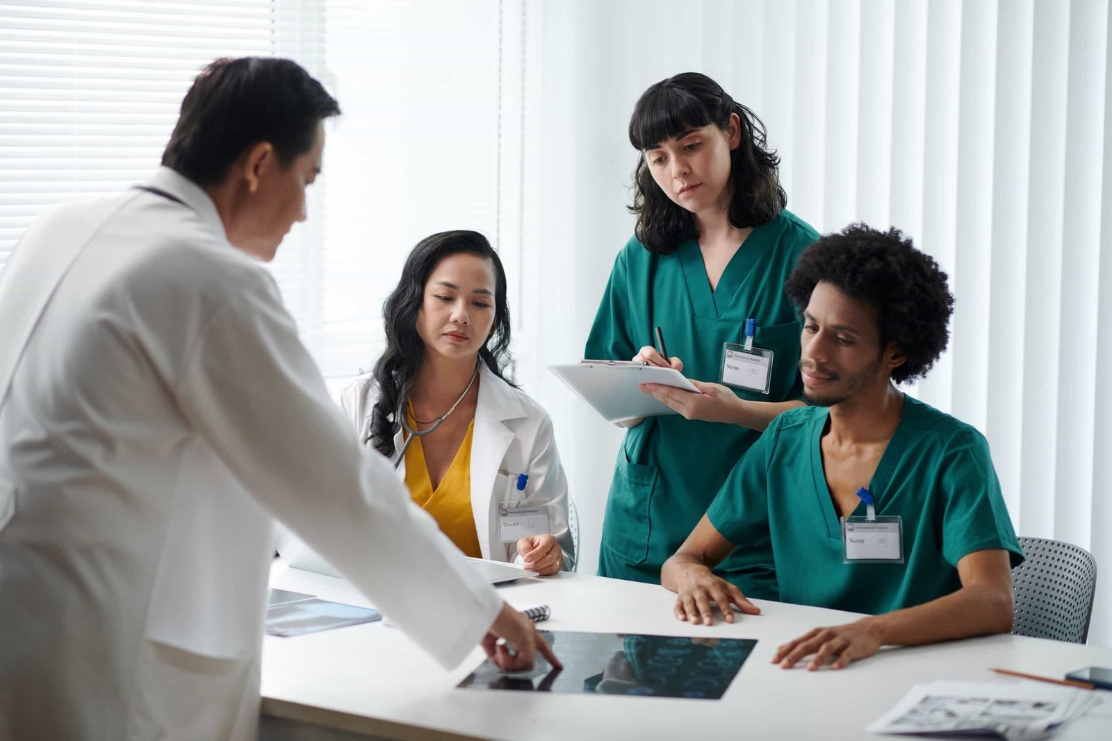 A group of medical professionals in scrubs and lab coats sit around a table reviewing X-rays and taking notes in a well-lit room. Medical Website redesign