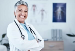 Smiling healthcare professional with short gray hair and a stethoscope stands with arms crossed in a medical office. seo for medical practices in nyc