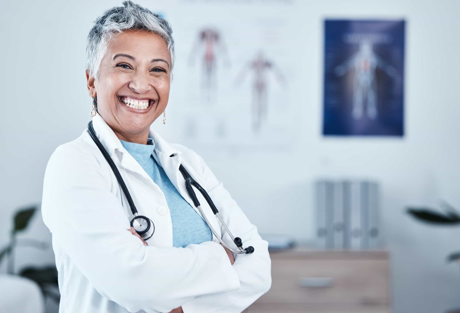 Smiling healthcare professional with short gray hair and a stethoscope stands with arms crossed in a medical office. seo for medical practices in nyc