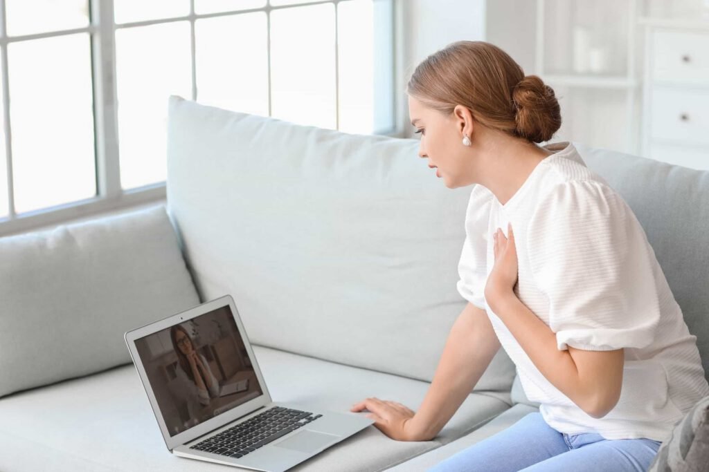 A woman sits on a couch having a video call on her laptop, with another woman visible on the laptop screen. Promise.