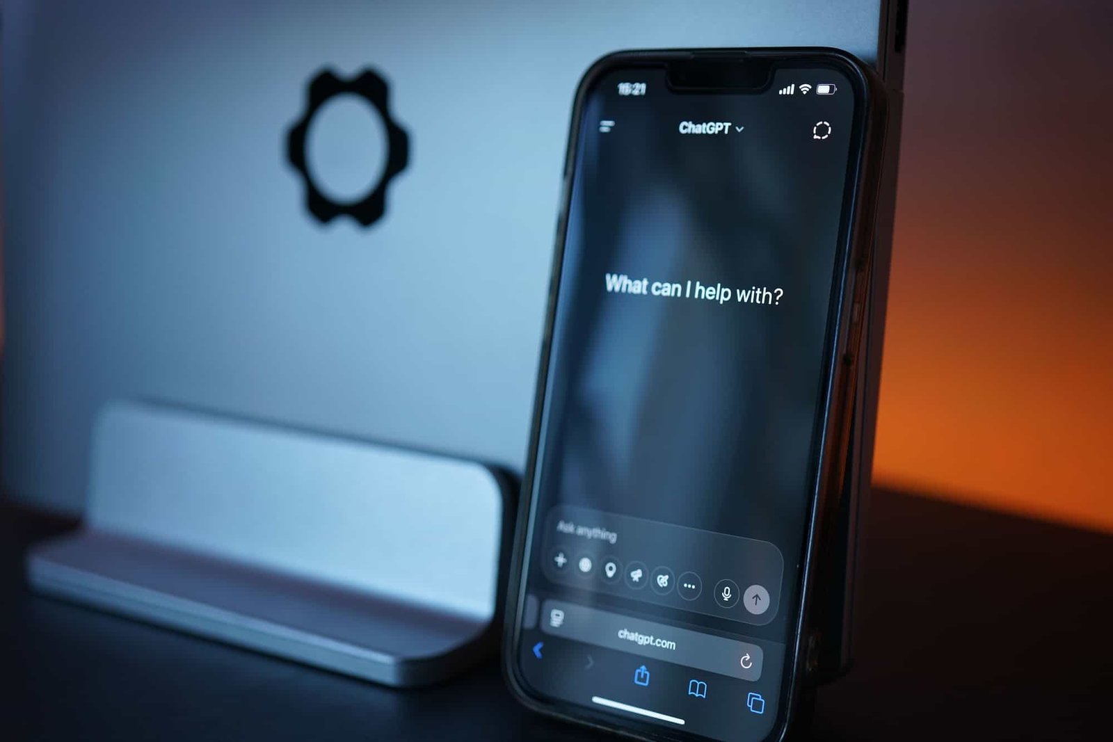 A smartphone displaying a ChatGPT interface that reads "What can I help with?" is propped up against a silver laptop with a gear symbol. Medical AI