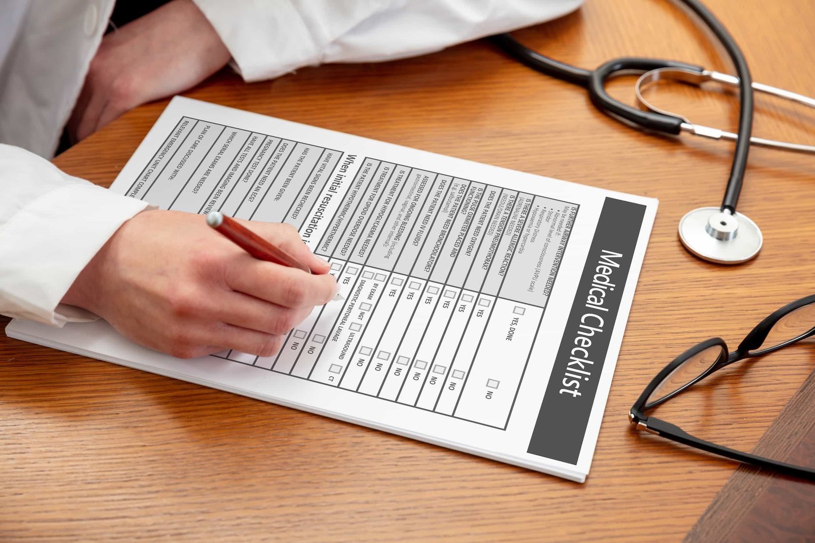A person fills out a medical checklist form on a clipboard at a desk, with a stethoscope and eyeglasses nearby. Medical Practice Website Checklist for Queens, NY