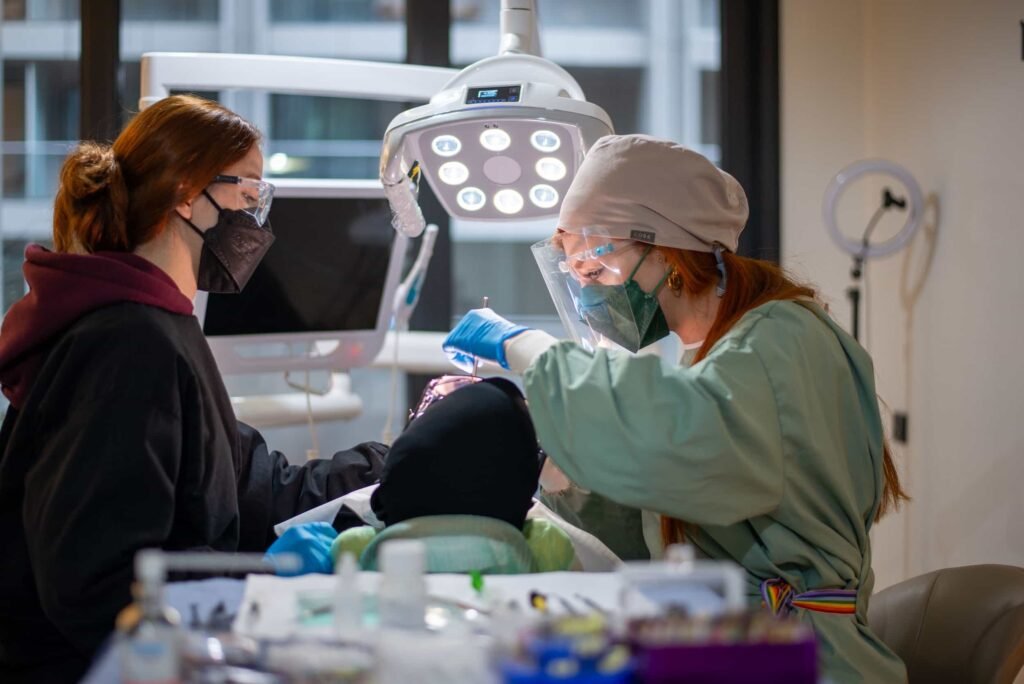 Two dental professionals wearing masks and protective gear perform a dental procedure on a patient in a brightly lit clinic. SEO for Dentists: How to Get More Patients From Googl. SEO for Dentists