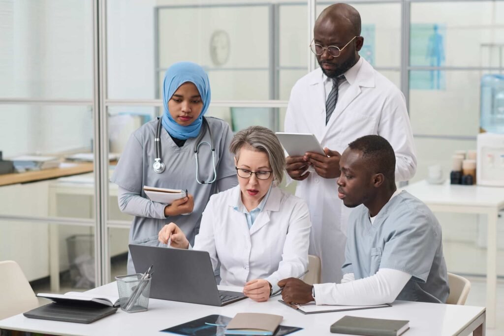 Four medical professionals review information together at a table, with laptops and documents in a modern office setting. Why Your EHR Website Isn't Bringing You New Patients