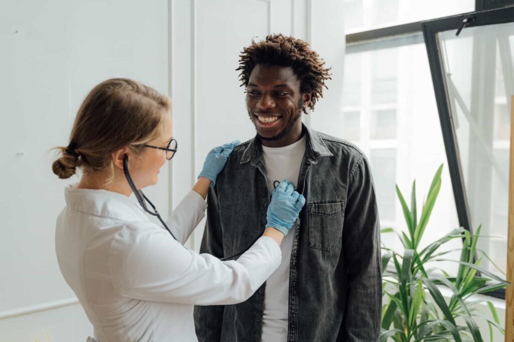 A healthcare professional uses a stethoscope to listen to a man’s chest while he stands and smiles in a medical office. Patient Acquisition