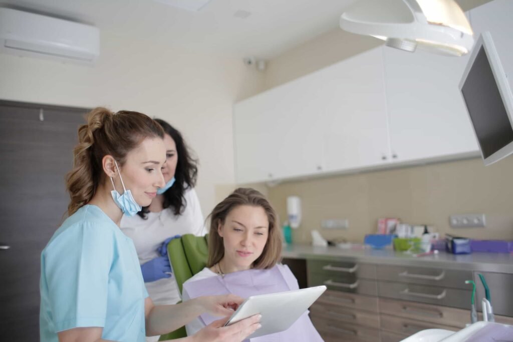 Two dental professionals show a patient something on a tablet in a modern dental clinic. The patient is seated in the dental chair, and the staff is wearing scrubs and masks. Dental SEO and web design in new york city