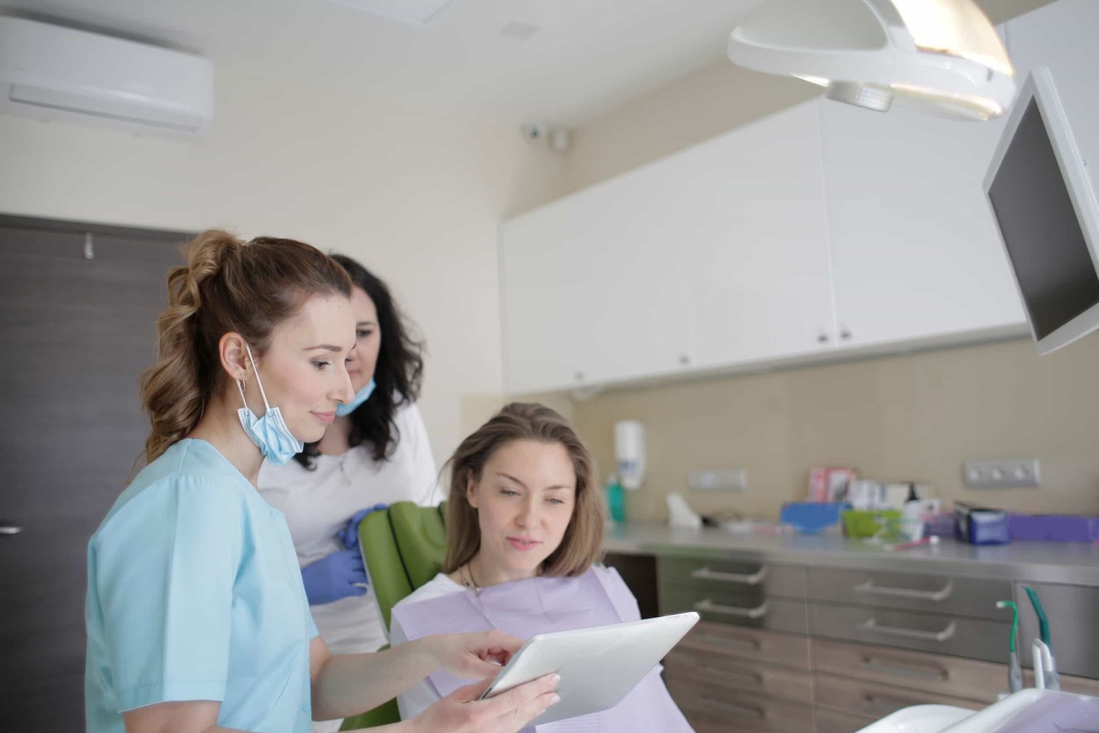 Two dental professionals show a patient something on a tablet in a modern dental clinic. The patient is seated in the dental chair, and the staff is wearing scrubs and masks. Dental SEO and web design in new york city