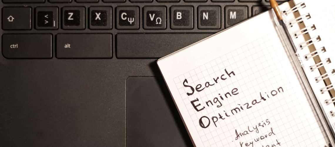 A notebook labeled "SEO Search Engine Optimization" with related keywords rests on a laptop keyboard with both English and Greek letters. 10 Essential Tips for Building a WordPress Site with SEO in Mind