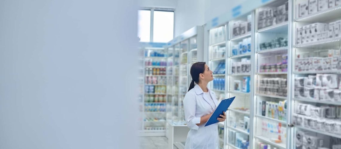 Pharmacist with a clipboard observes shelves of medicine and products in a pharmacy.