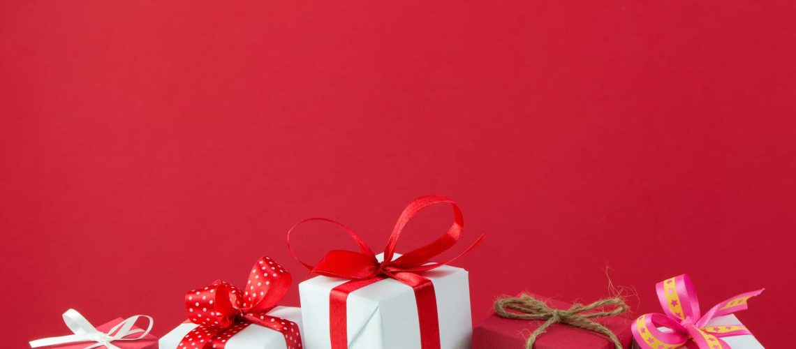 Five wrapped gift boxes with red and white ribbons and bows are arranged on a layer of artificial snow against a plain red background. Discover essential tips to optimize your WordPress site for Black Friday 2025. Boost traffic and sales with our comprehensive guide.