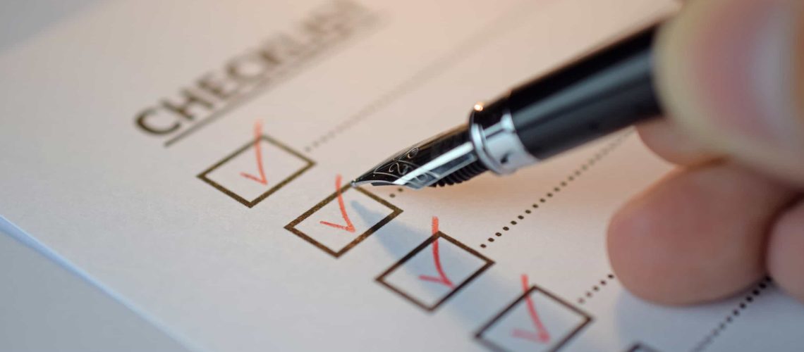 A hand holding a pen checks off boxes on a paper checklist, with several boxes already marked with red checkmarks. The Simple SEO Checklist for Small Business Websites