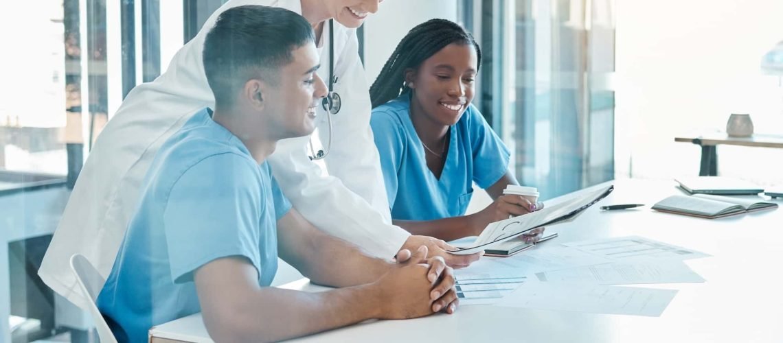 A doctor and two healthcare professionals in scrubs discuss documents at a table in a bright room.