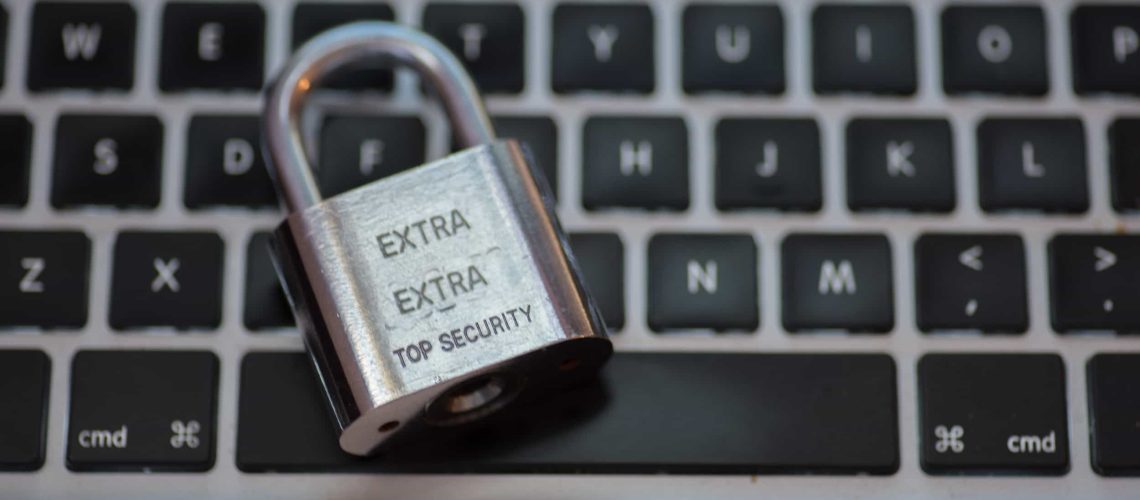A metal padlock labeled "EXTRA EXTRA TOP SECURITY" rests on a laptop keyboard.